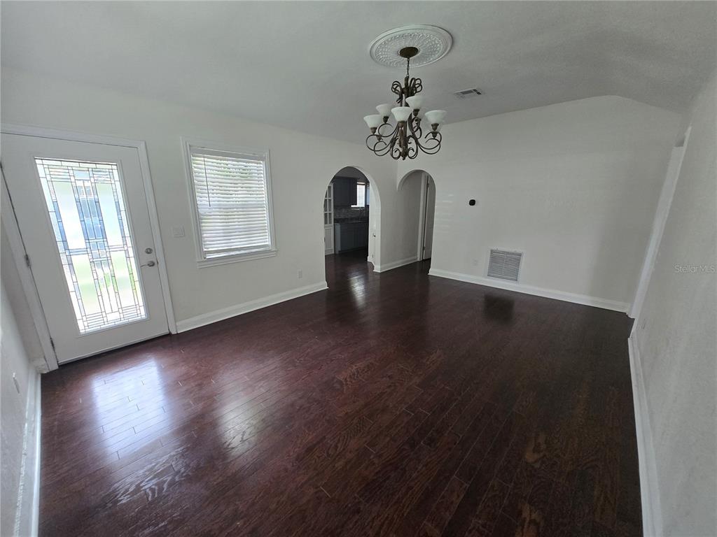 A dining room features dark hardwood floors, a chandelier, and arched doorways leading to a kitchen — 300 E IDLEWILD AVENUE, TAMPA, FL