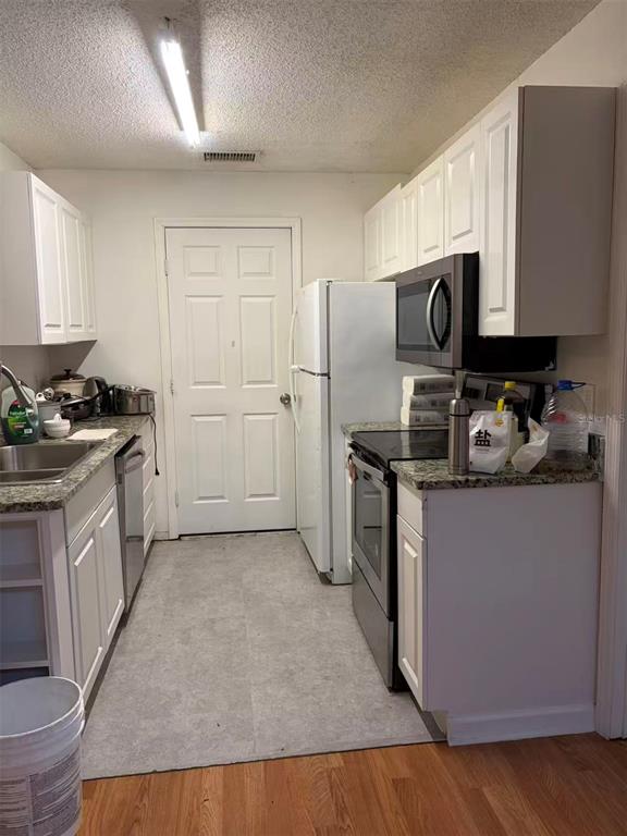 A galley kitchen features white cabinets, granite countertops, stainless steel appliances, and light-colored flooring — 1160 WOODMAN WAY, ORLANDO, FL