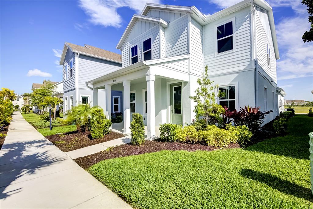 A light blue two-story house with a covered front porch and a concrete sidewalk — 9116 WALCOTT LANE, SARASOTA, FL
