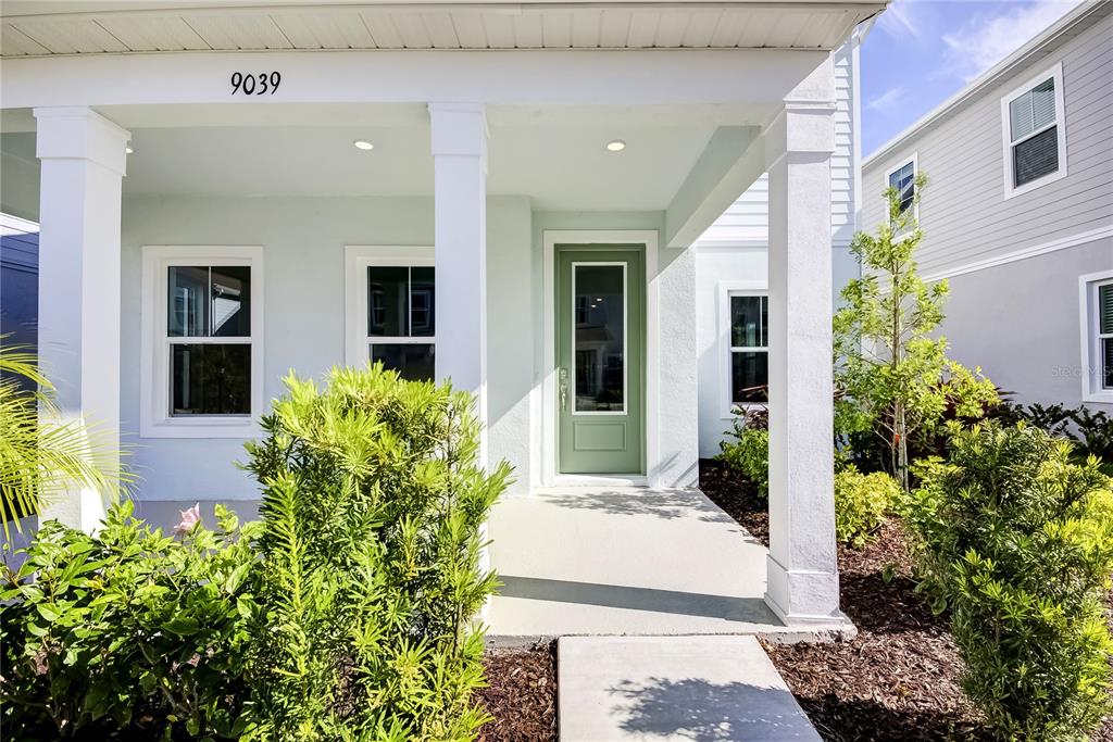 A light blue house exterior features a covered front porch with white columns and green door — 9116 WALCOTT LANE, SARASOTA, FL