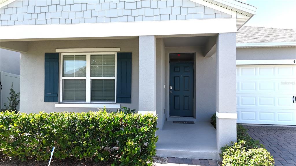 The exterior of a house features a blue front door, a window with shutters, and landscaping — 5425 PALOMINO PL, APOPKA, FL