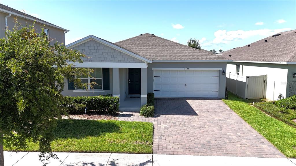 A single-story house with a gray shingle roof, a white garage door, and a paver driveway — 5425 PALOMINO PL, APOPKA, FL