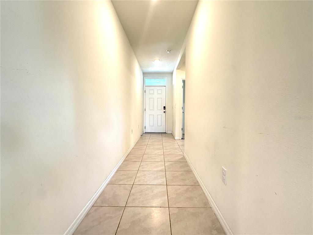 A long, narrow hallway with light-colored tile flooring leads to a white front door — 5425 PALOMINO PL, APOPKA, FL