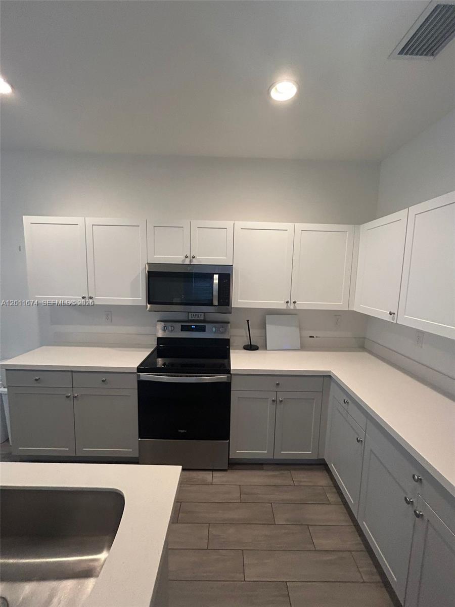 A kitchen features white cabinets, stainless steel appliances, and light-colored countertops over gray flooring — 5541 AGOSTINO WAY # 5541, Ave Maria FL 34142, AVE MARIA, FL