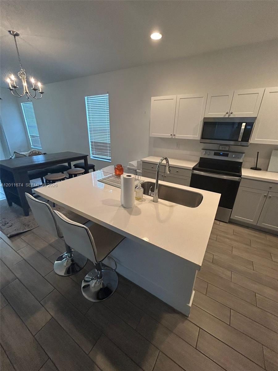 A kitchen features a white quartz island with a sink, white cabinets, and wood-look flooring — 5541 AGOSTINO WAY # 5541, Ave Maria FL 34142, AVE MARIA, FL