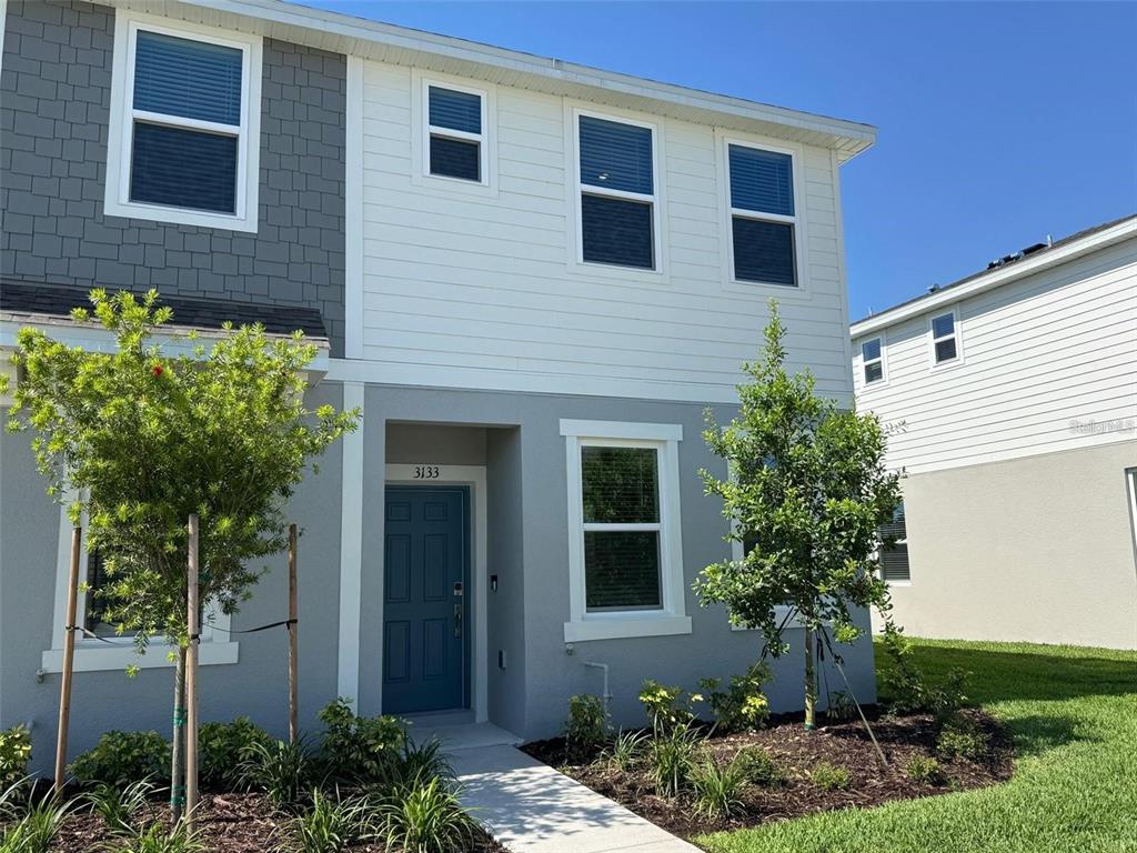 A two-story house exterior with gray and white siding, a blue front door, and landscaping — 3133 SKYLINE LOOP, KISSIMMEE, FL