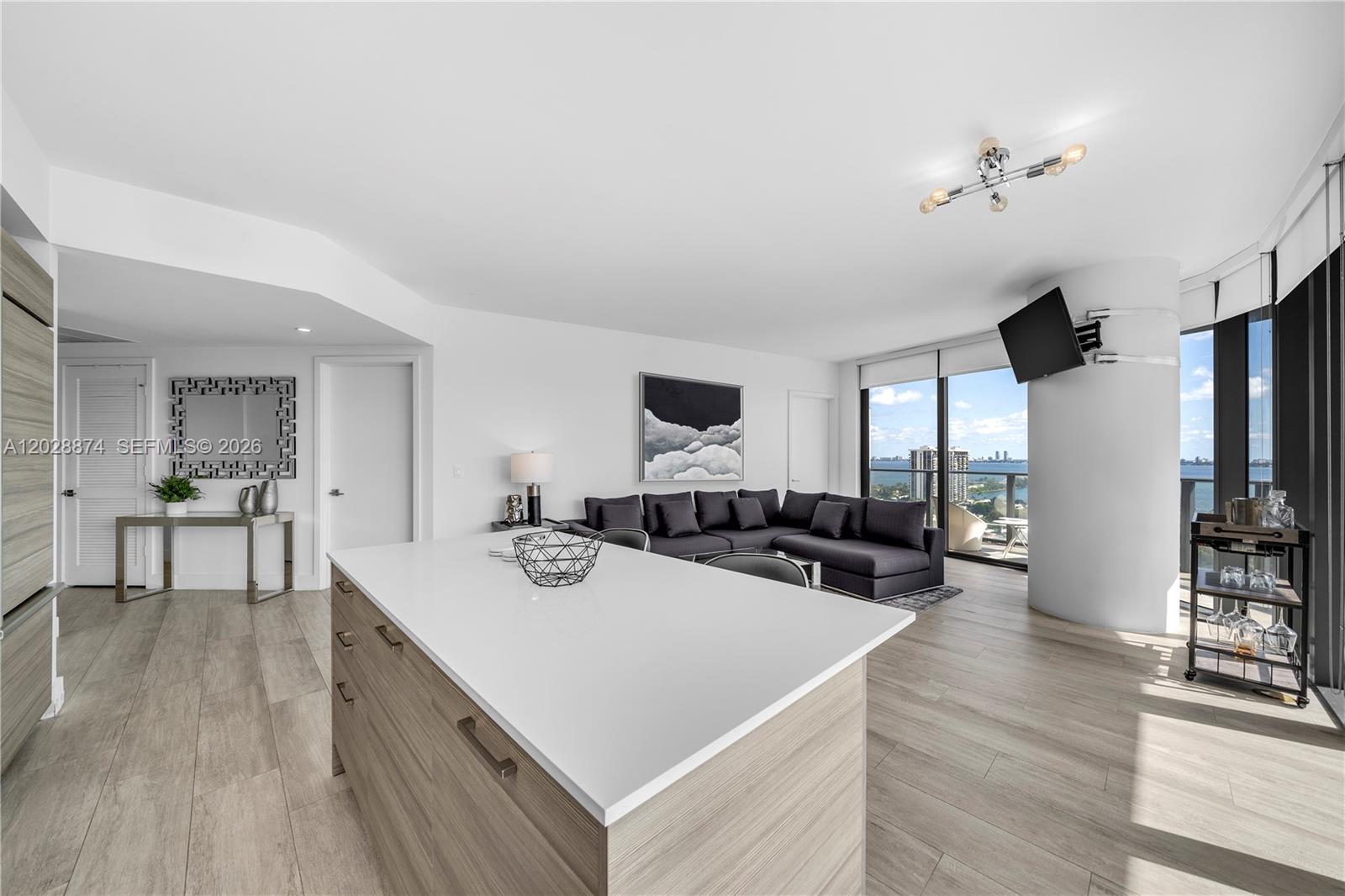 A modern living room and kitchen area features a large island, sectional sofa, and balcony — 121 NE 34th St # 1704, Miami FL 33137, MIAMI, FL
