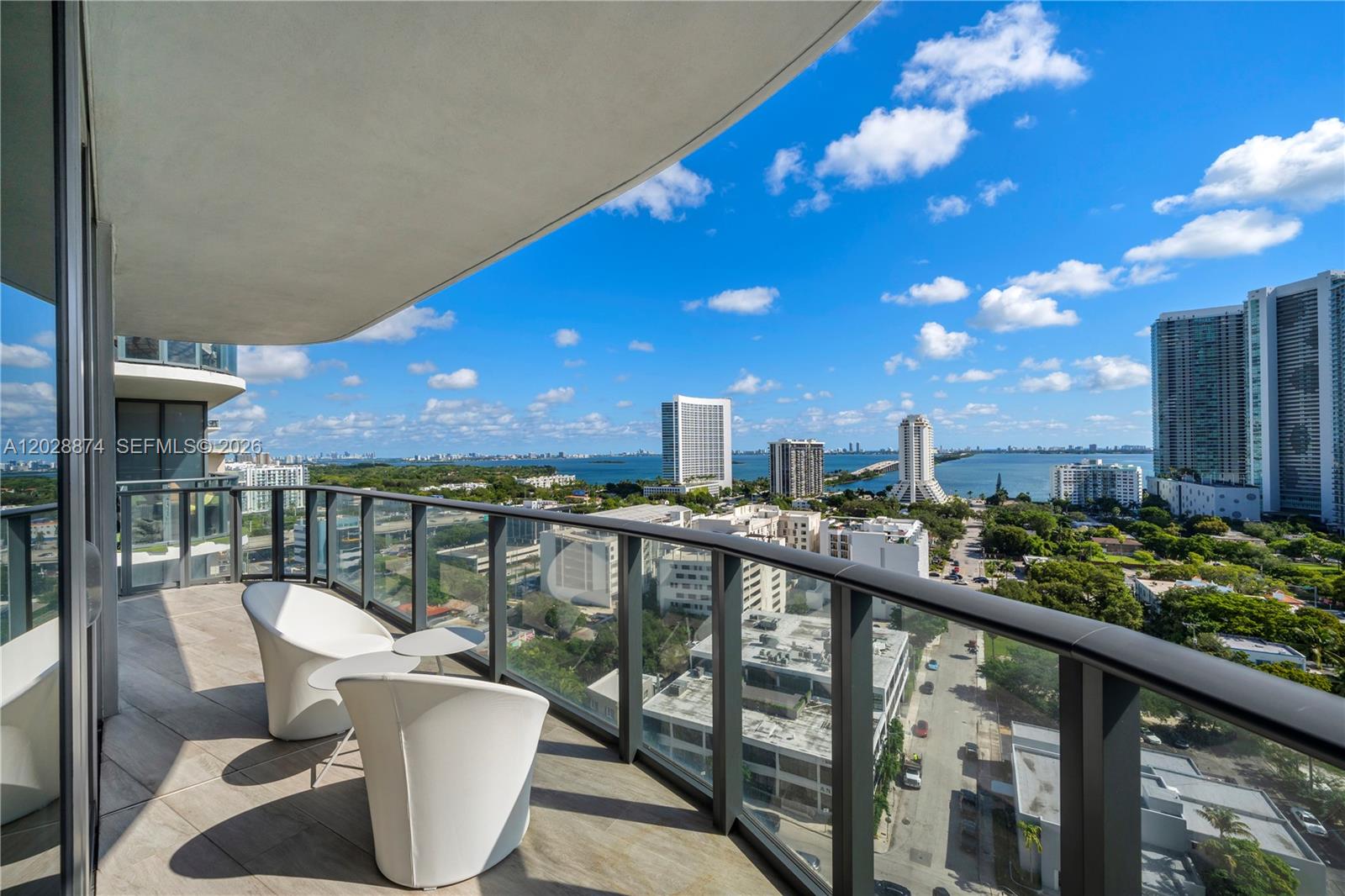 A high-rise balcony with two white chairs overlooks a city skyline and a bay — 121 NE 34th St # 1704, Miami FL 33137, MIAMI, FL