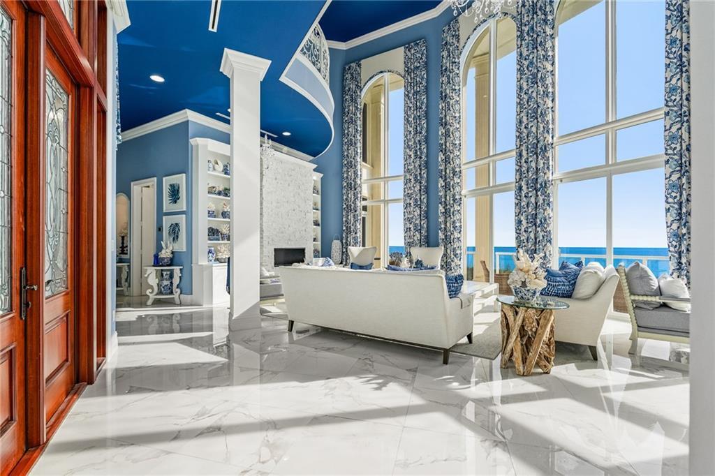A bright living room features blue ceilings, white marble floors, and floor-to-ceiling windows overlooking water — FORT PIERCE, FL