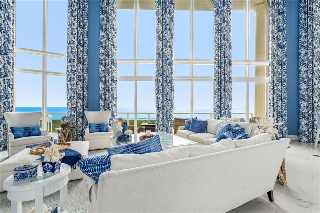 A bright living room features floor-to-ceiling windows with ocean views and blue floral curtains — FORT PIERCE, FL