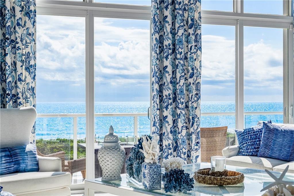 A living room with blue floral curtains overlooks the ocean through large floor-to-ceiling windows — FORT PIERCE, FL