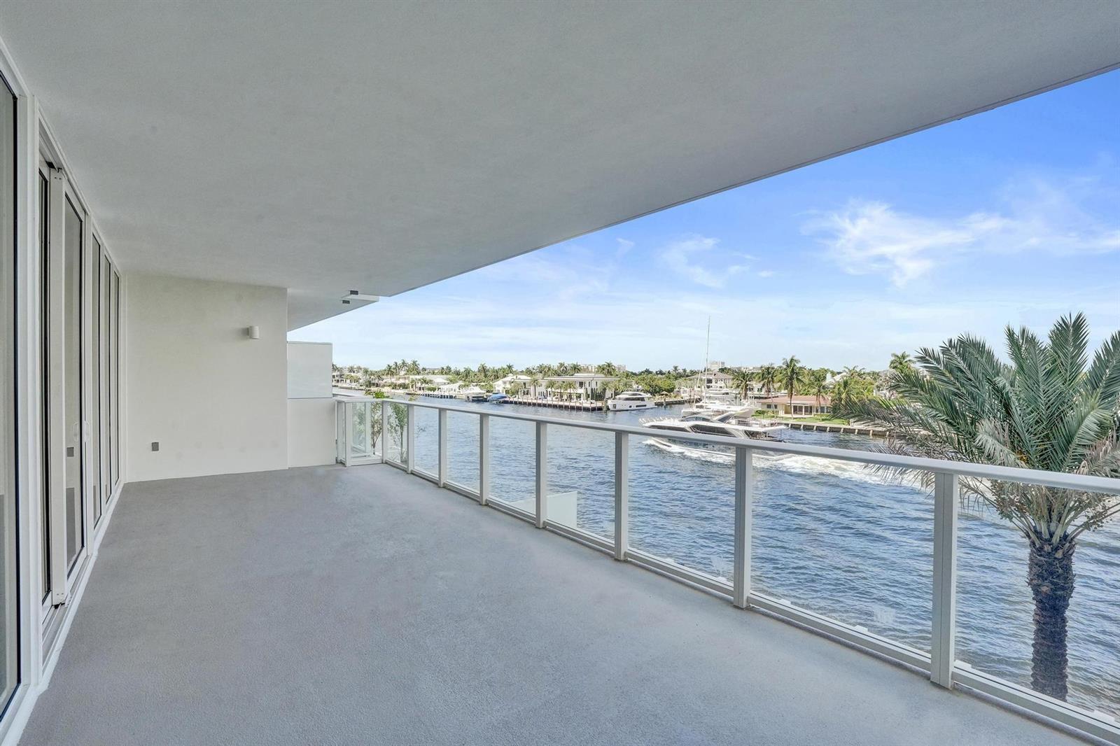 A spacious balcony with a glass railing overlooks a canal with boats and palm trees — 407 N Riverside Drive # 303, Pompano Beach FL 33062, POMPANO BEACH, FL