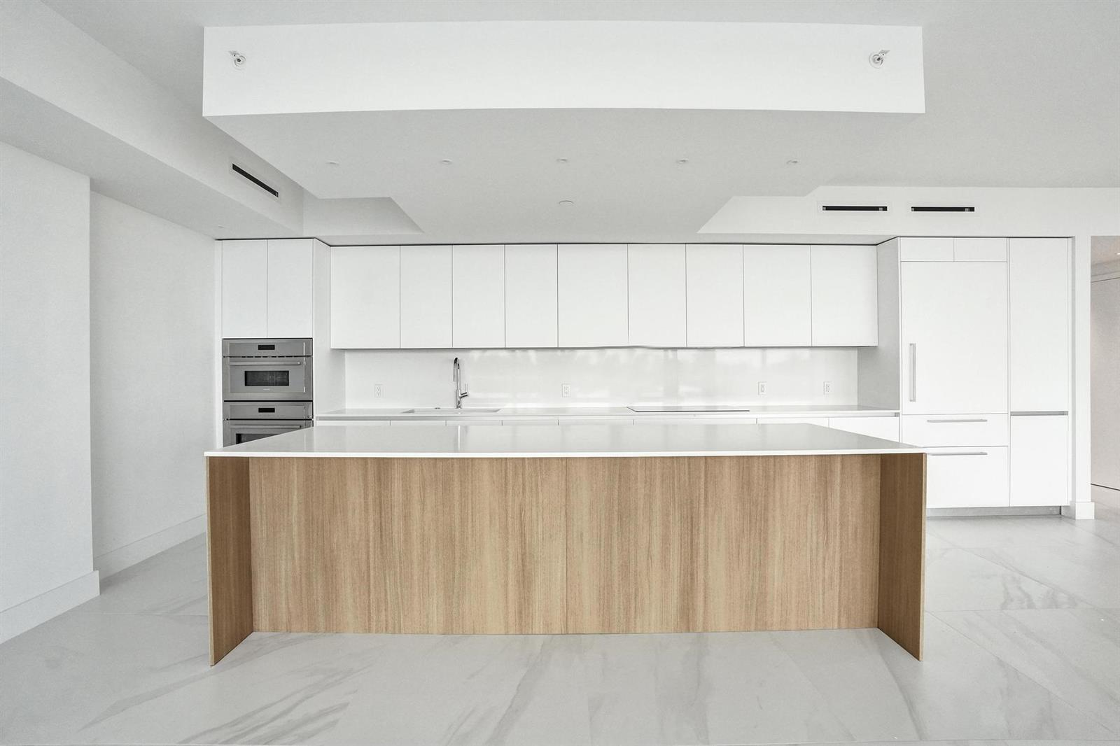 A modern kitchen features white cabinetry, a light wood island, and white marble-style flooring — 407 N Riverside Drive # 303, Pompano Beach FL 33062, POMPANO BEACH, FL