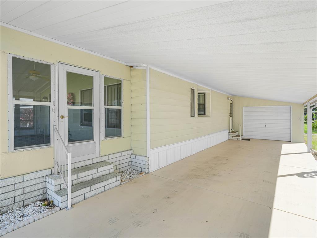 A pale yellow mobile home features a covered carport, concrete driveway, and white brick steps — 134 LAKE HAZEL DRIVE, WINTER HAVEN, FL