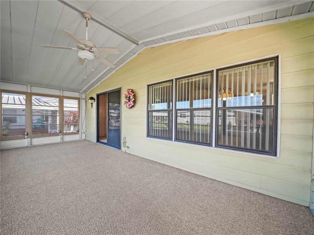 A covered patio features beige siding, a ceiling fan, carpeted flooring, and large windows — 134 LAKE HAZEL DRIVE, WINTER HAVEN, FL