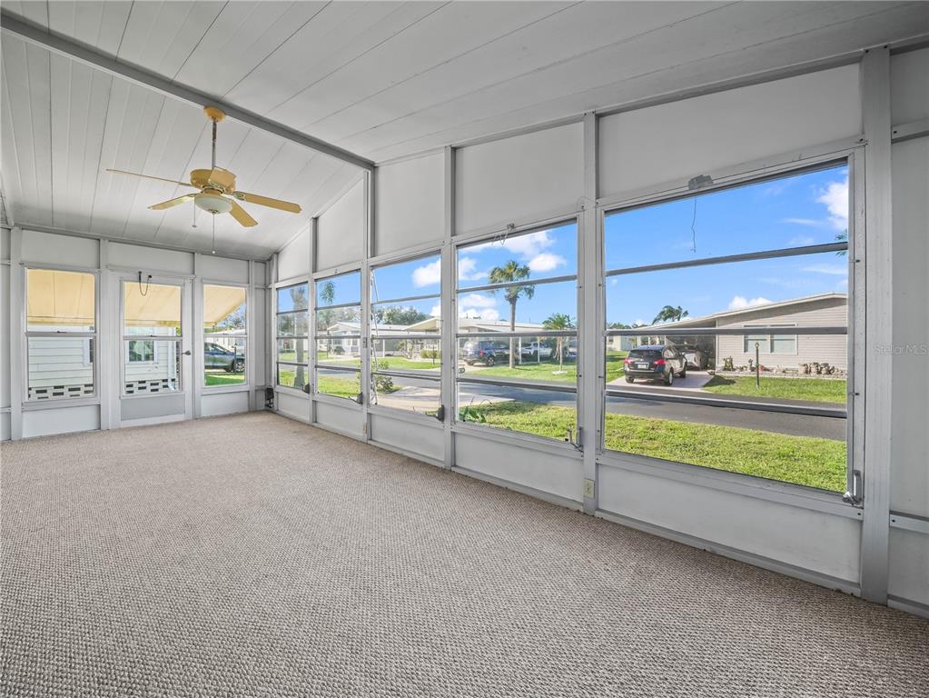 A carpeted sunroom features a ceiling fan and large screened windows overlooking a residential street — 134 LAKE HAZEL DRIVE, WINTER HAVEN, FL