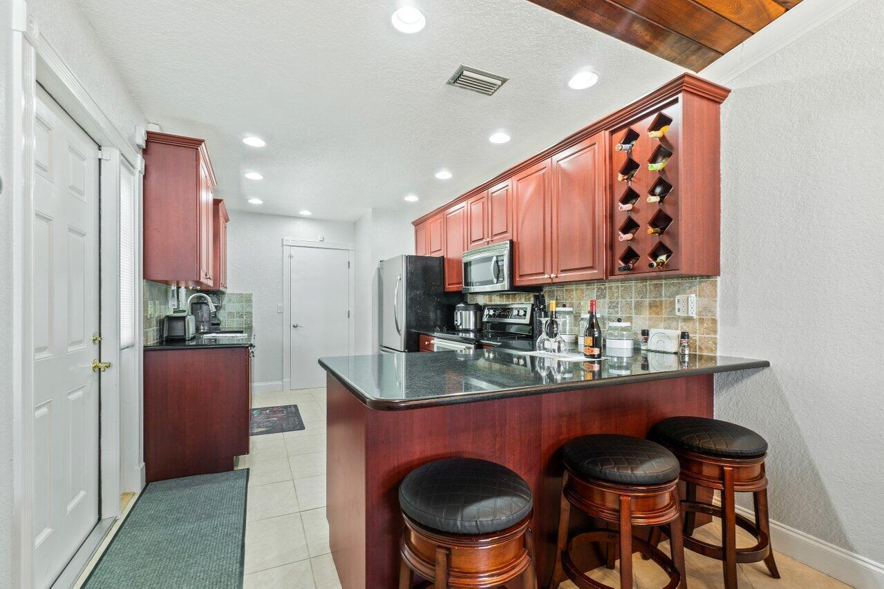 A kitchen features cherry wood cabinets, black granite countertops, a breakfast bar, and tile flooring — 12542 Westhampton Circle, Wellington FL 33414, WELLINGTON, FL
