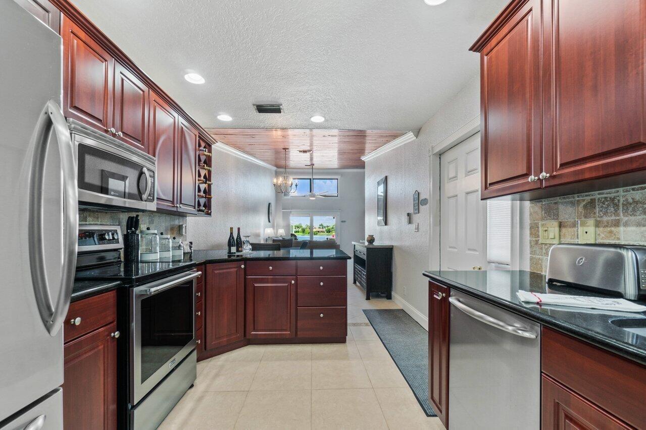 A kitchen with dark wood cabinets, black countertops, stainless steel appliances, and a wood-paneled ceiling — 12542 Westhampton Circle, Wellington FL 33414, WELLINGTON, FL