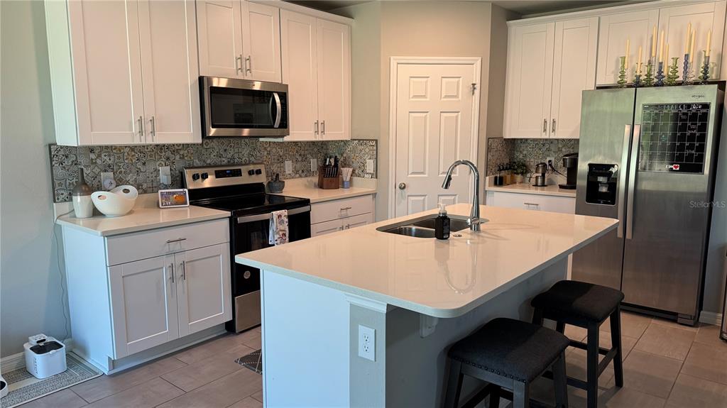 A kitchen features white cabinetry, a central island with seating, and a patterned tile backsplash — 17268 CAGAN CROSSINGS BOULEVARD, CLERMONT, FL