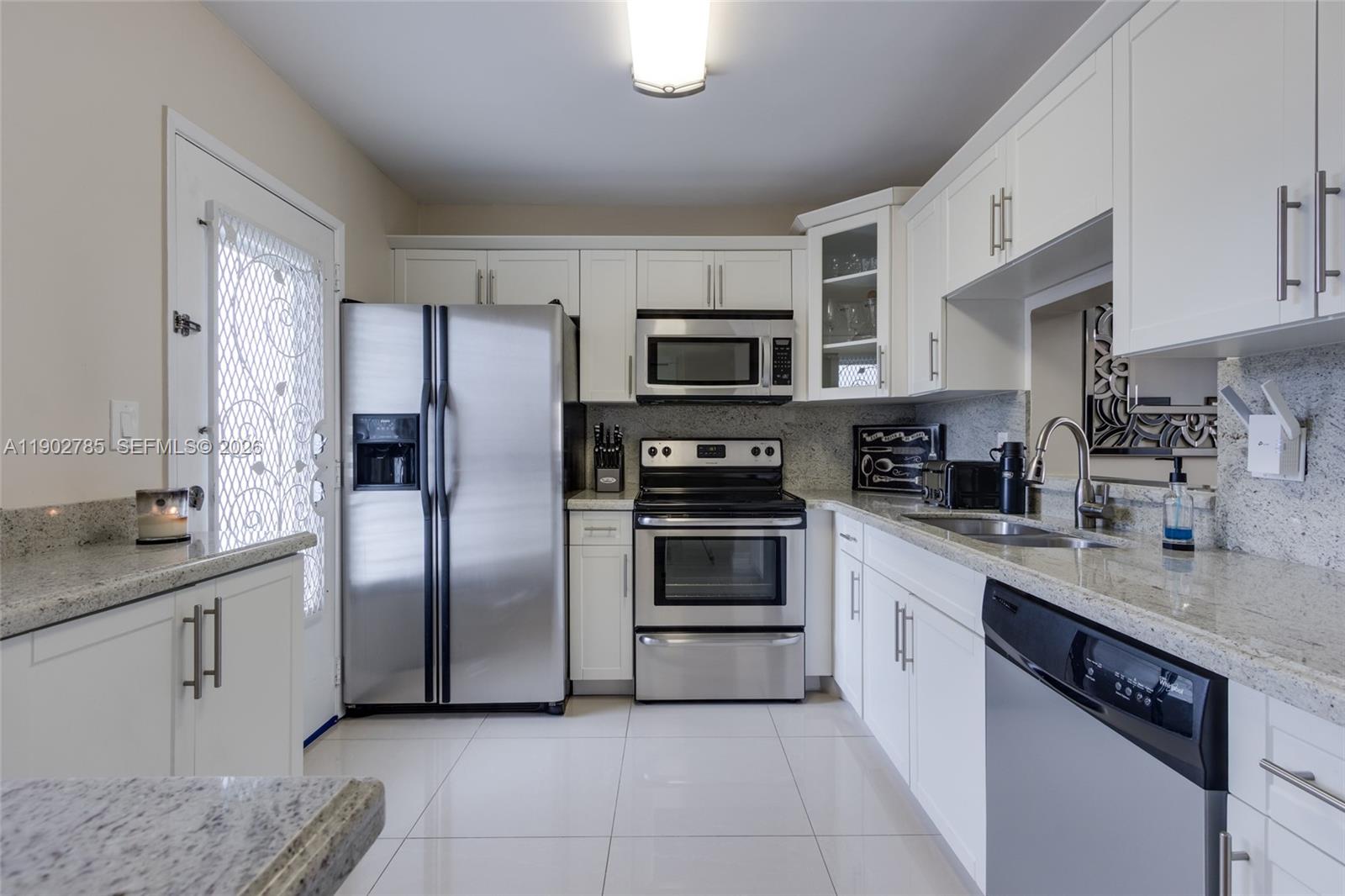 A kitchen features white cabinets, stainless steel appliances, and granite countertops with tile flooring — 420 NE 12th Ave # 208, Hallandale Beach FL 33009, HALLANDALE BEACH, FL