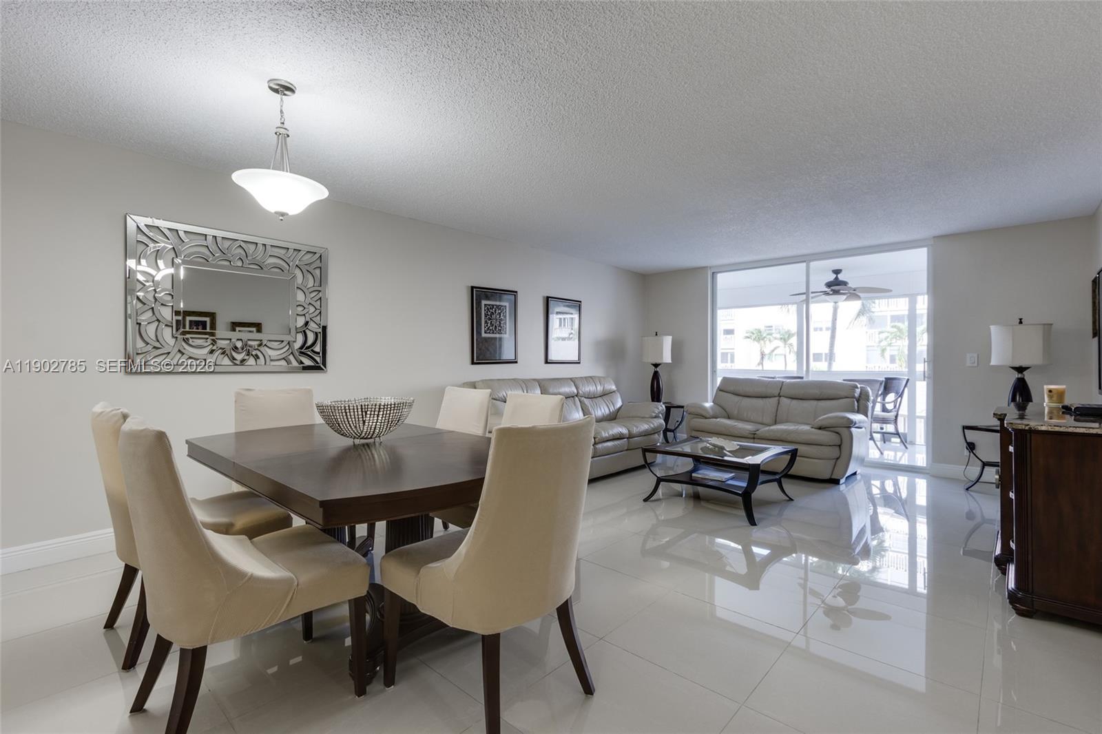 A dining area and living room feature white tile floors, neutral walls, and sliding glass doors — 420 NE 12th Ave # 208, Hallandale Beach FL 33009, HALLANDALE BEACH, FL
