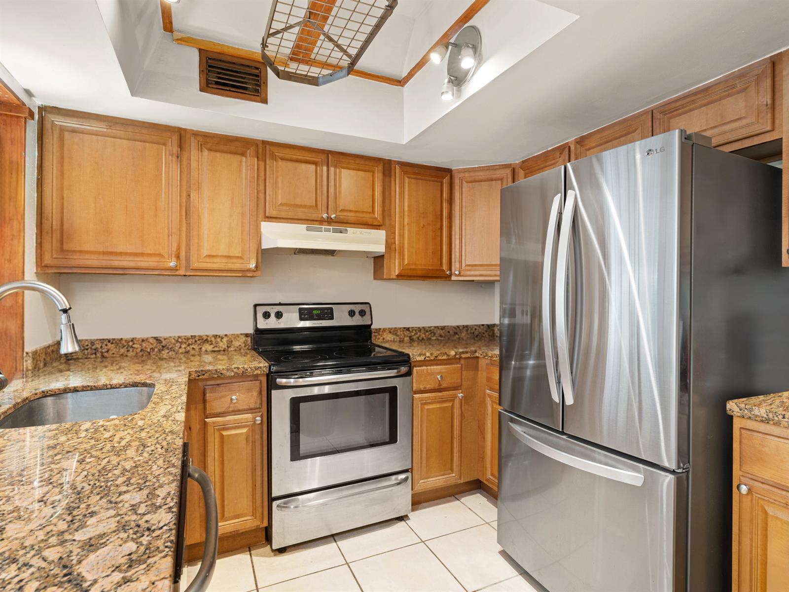 A kitchen features wooden cabinets, granite countertops, stainless steel appliances, and a tiled floor — 811 SE 4th Avenue # C103, Dania Beach FL 33004, DANIA BEACH, FL