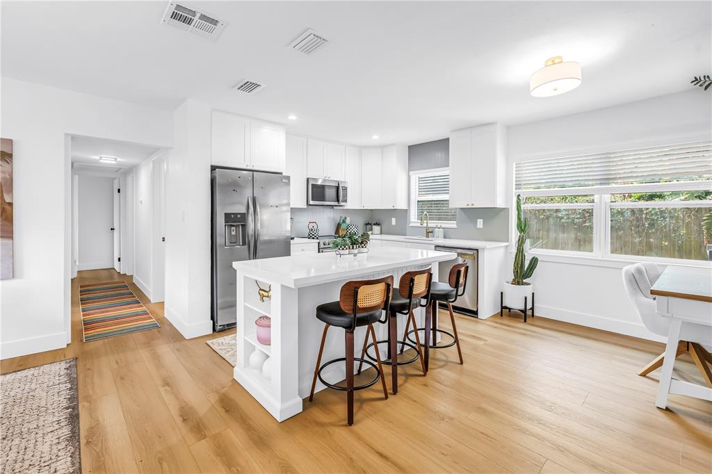 A modern kitchen features white cabinetry, a central island with bar seating, and wood flooring — 7400 19TH AVENUE N, ST PETERSBURG, FL