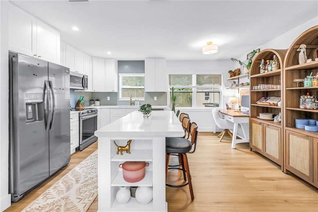 A bright kitchen features white cabinetry, a central island, stainless appliances, and a workspace area — 7400 19TH AVENUE N, ST PETERSBURG, FL
