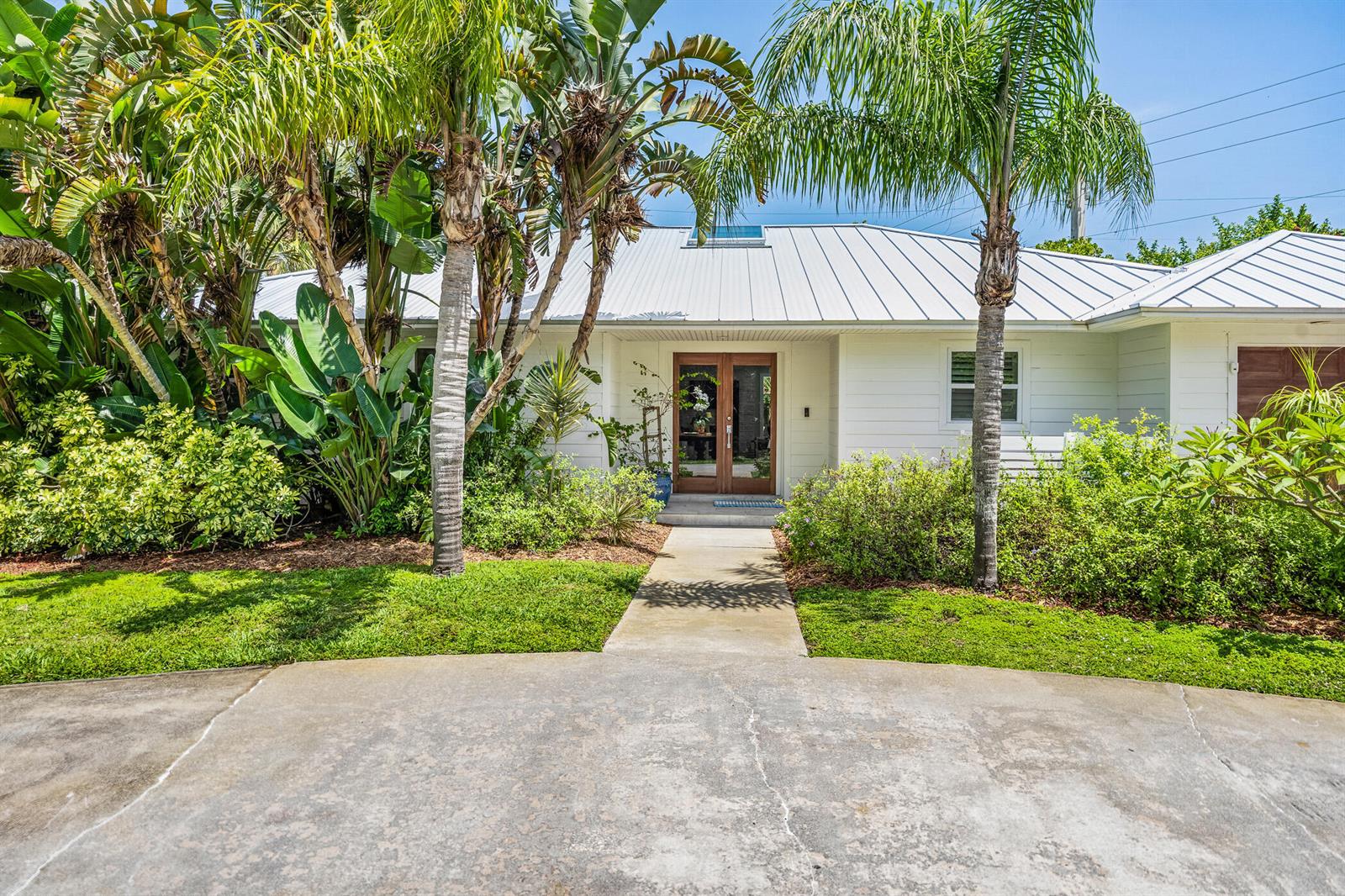 A white house with a metal roof and double front doors sits behind a walkway — VERO BEACH, FL