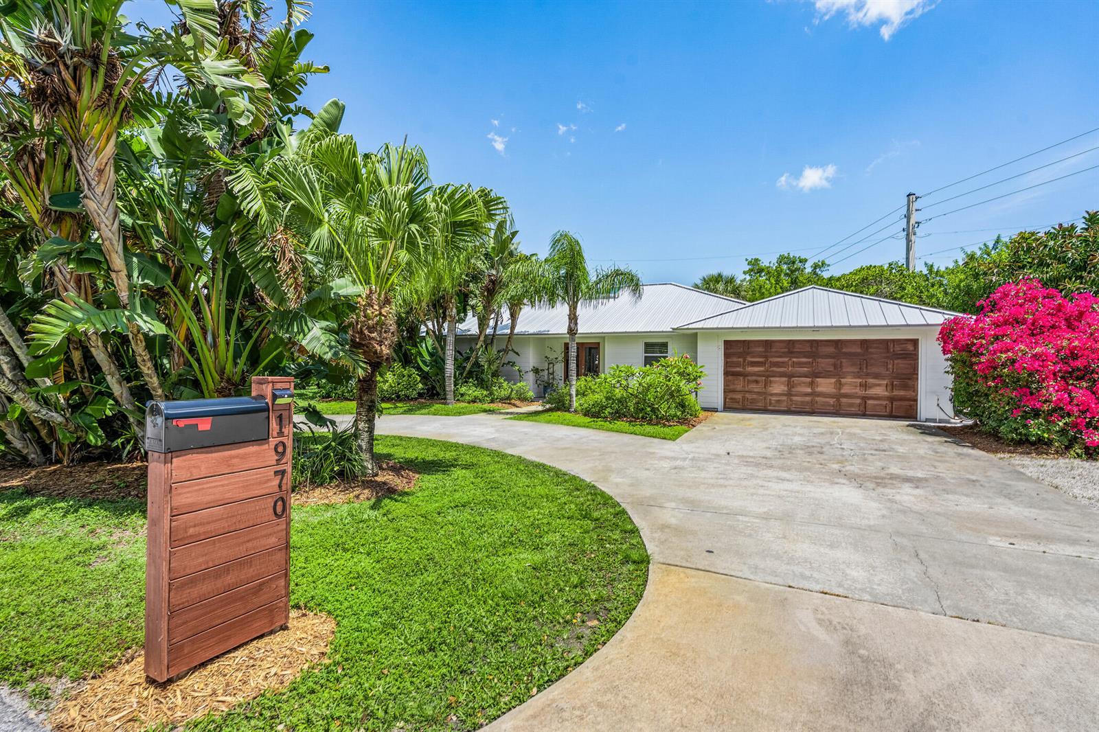 A white house with a metal roof and a wooden garage door sits behind a driveway — VERO BEACH, FL