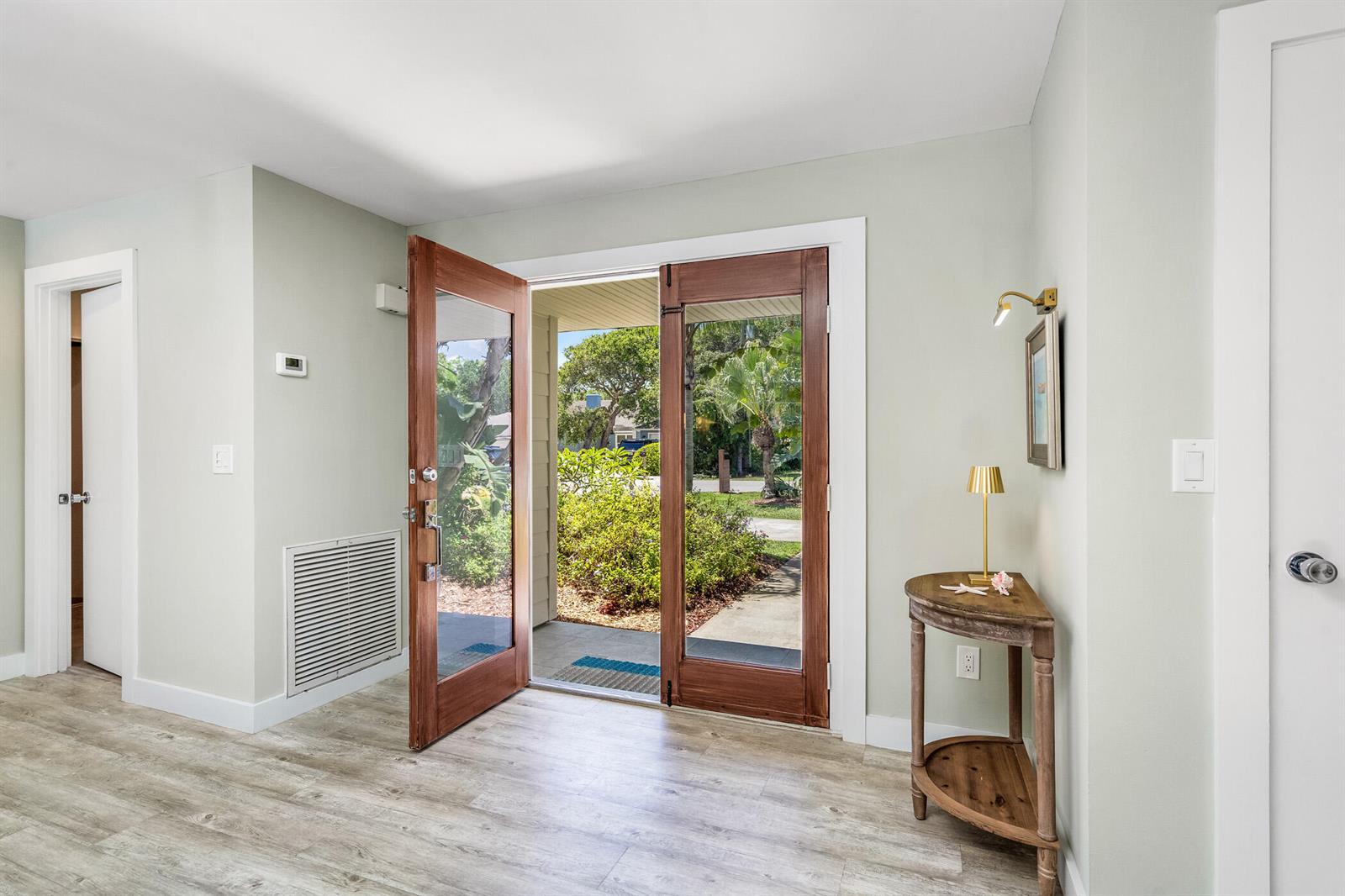 An entryway features light wood-look flooring, a half-moon table, and double glass-paneled wooden doors — VERO BEACH, FL