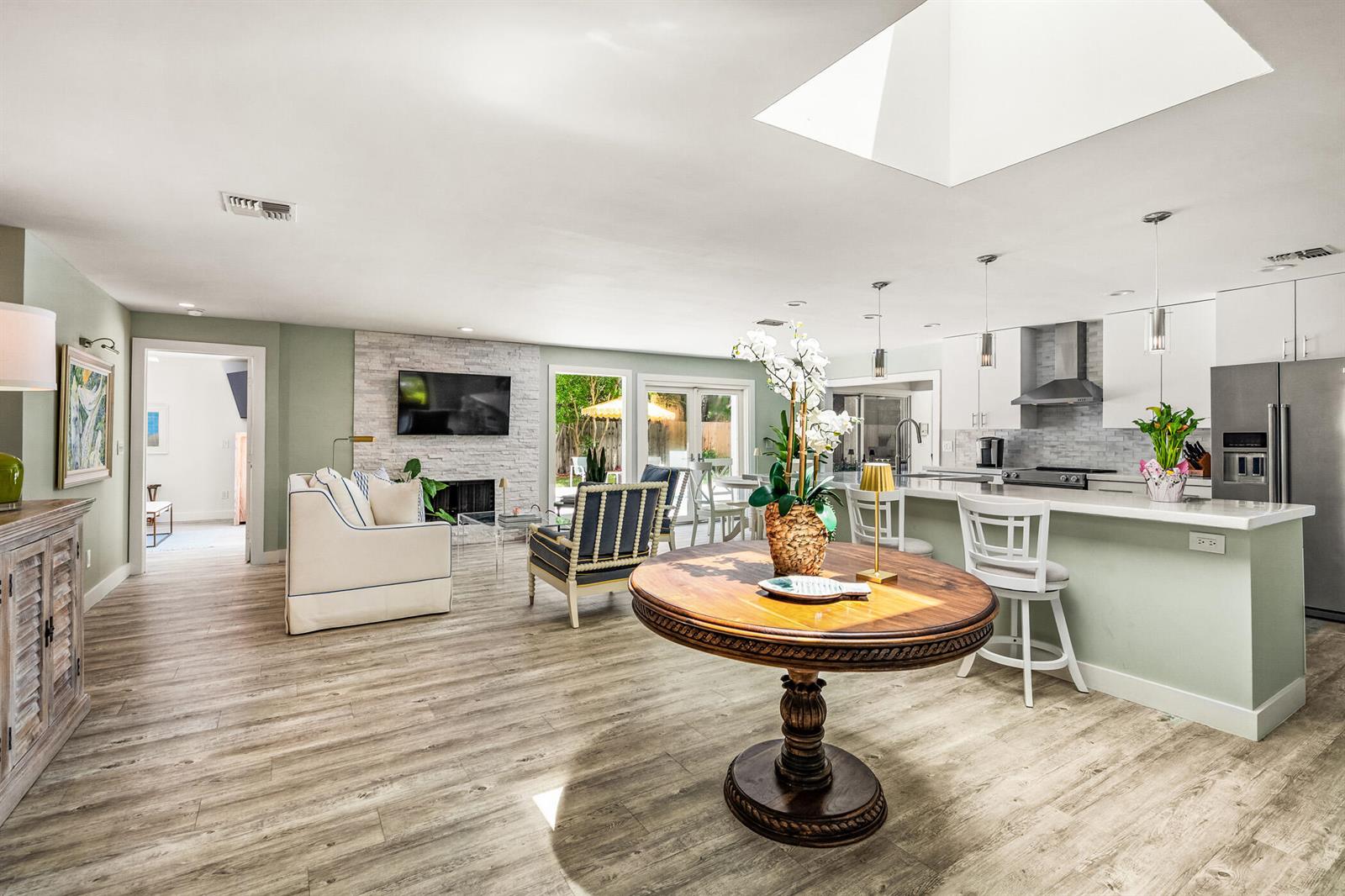 An open-concept living room and kitchen featuring a stone fireplace, skylight, and wood-look flooring — VERO BEACH, FL