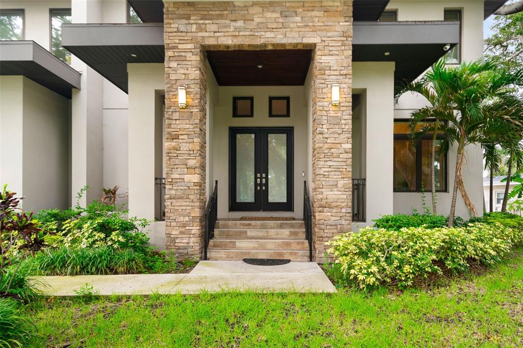 The exterior of a modern home features a stone-clad entryway with double glass doors — 4905 W SPRING LAKE DRIVE, TAMPA, FL