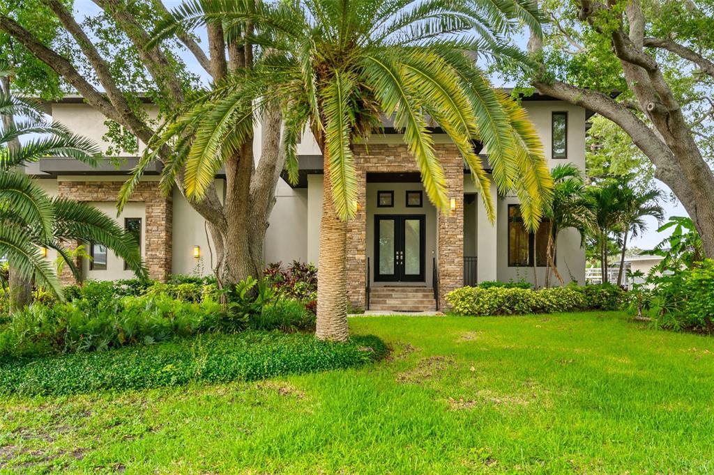 A two-story house with a stone facade, a palm tree, and a lush green lawn — 4905 W SPRING LAKE DRIVE, TAMPA, FL