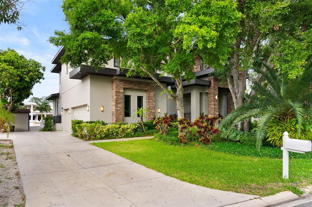 A two-story house with stone accents, a concrete driveway, and mature trees in the yard — 4905 W SPRING LAKE DRIVE, TAMPA, FL