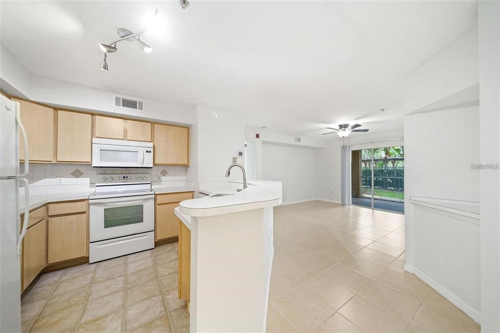 A kitchen with light wood cabinets and white appliances opens to a tiled living area — 823 CAMARGO WAY UNIT 104, ALTAMONTE SPRINGS, FL