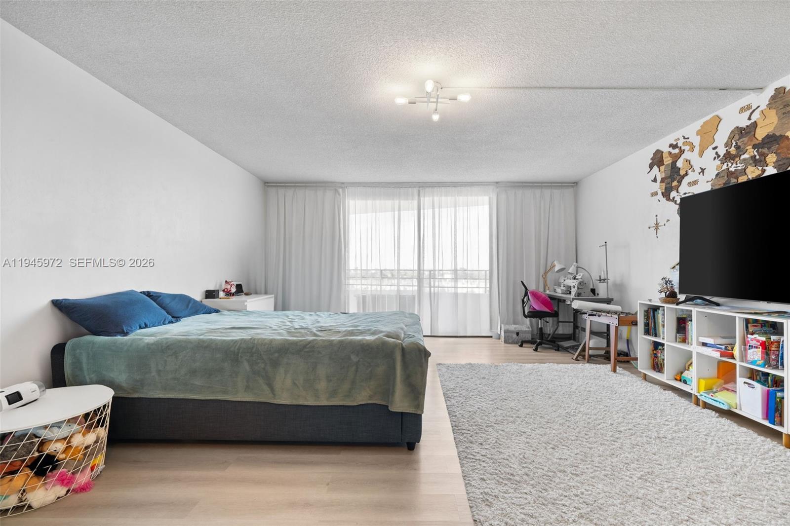 A bedroom features a bed, a desk, a television on a shelf, and a large window — 600 Three Islands Blvd # 606, Hallandale Beach FL 33009, HALLANDALE BEACH, FL