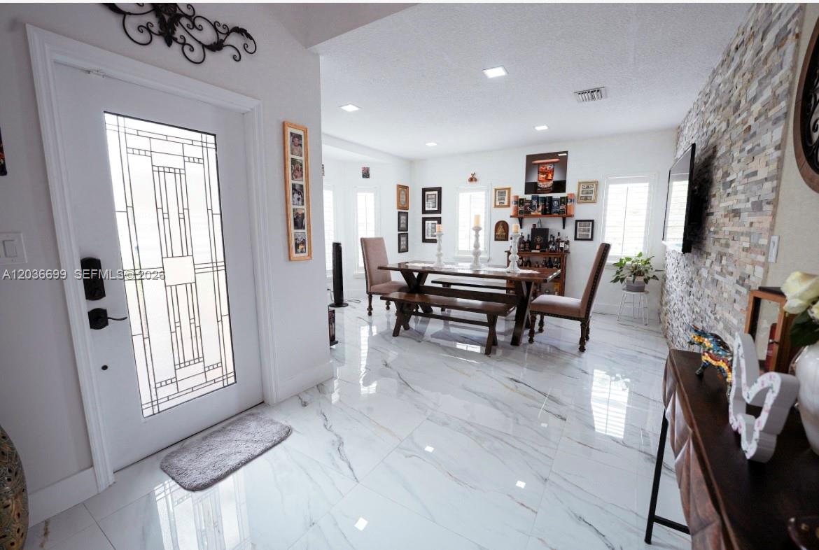 A dining room features white marble floors, a stone accent wall, and a glass-paneled front door — 1935 NE 35th Ave, Homestead FL 33033, HOMESTEAD, FL