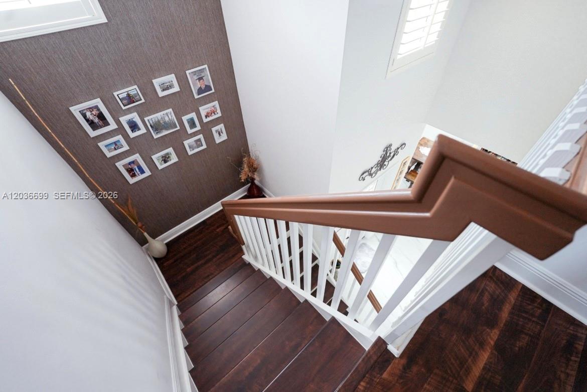 A wooden staircase with white railings leads down past a wall decorated with framed photos — 1935 NE 35th Ave, Homestead FL 33033, HOMESTEAD, FL