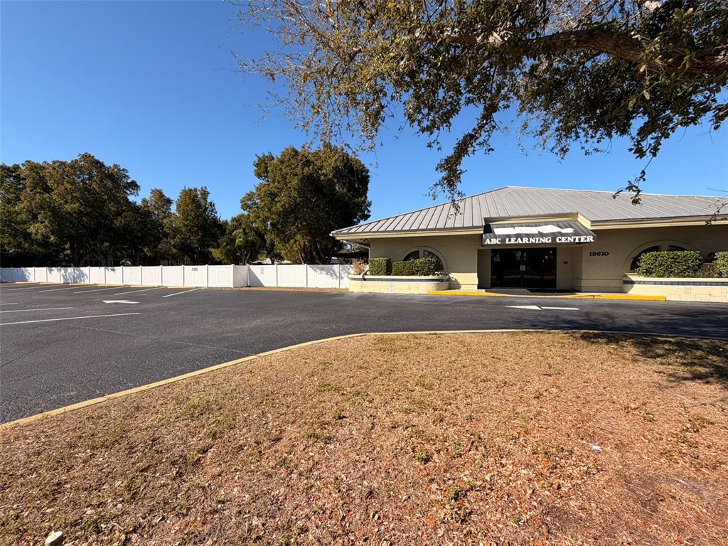 The exterior of a single-story commercial building with a parking lot and white privacy fence — 13610 LEARNING COURT, FORT MYERS, FL