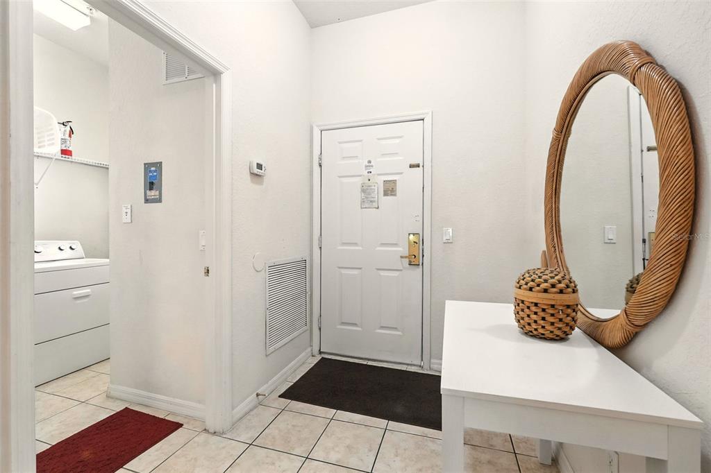 An entryway with white walls, tiled floors, a white console table, and a rattan-framed mirror — 809 GRAN BAHAMA BOULEVARD UNIT 30809, DAVENPORT, FL