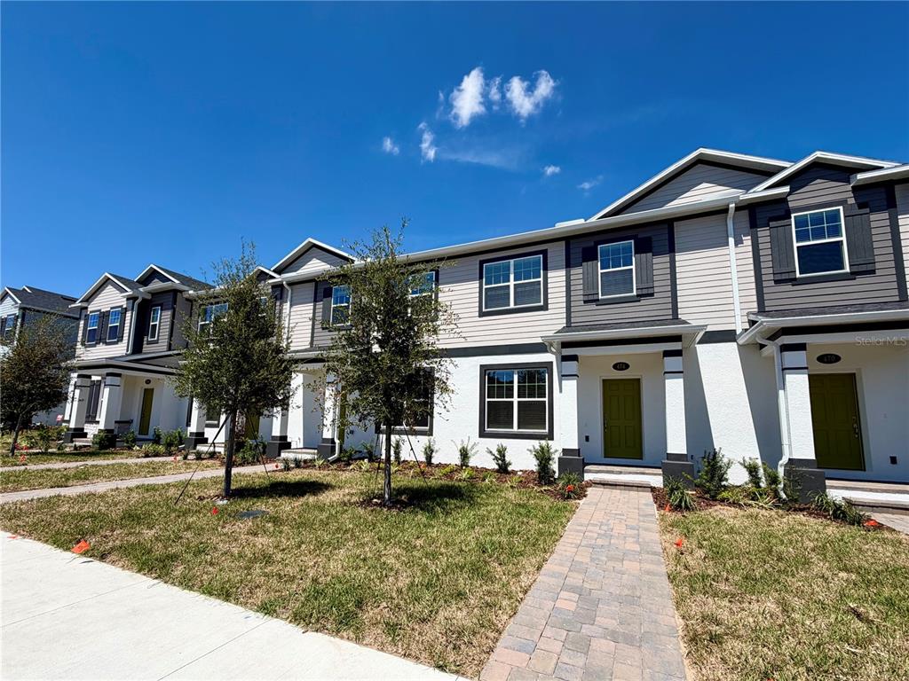 A row of two-story townhomes features white stucco, gray siding, and green front doors — 474 LADY PALM STREET, APOPKA, FL