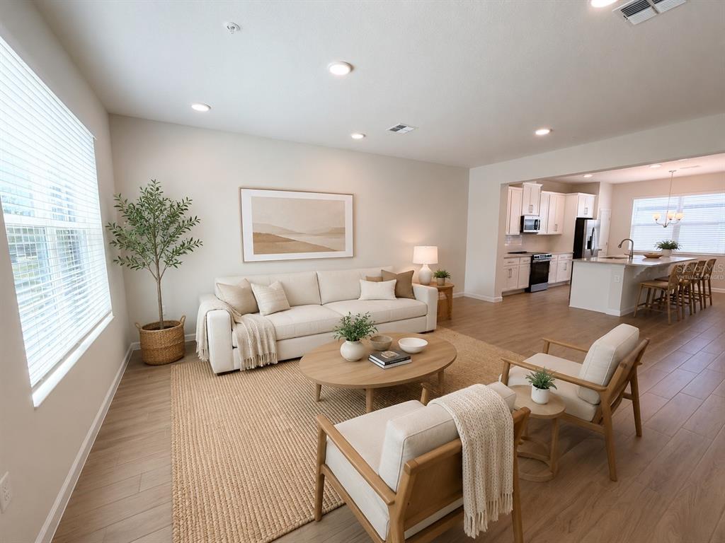 A bright living room with light wood floors, a beige sofa, and an open kitchen — 474 LADY PALM STREET, APOPKA, FL