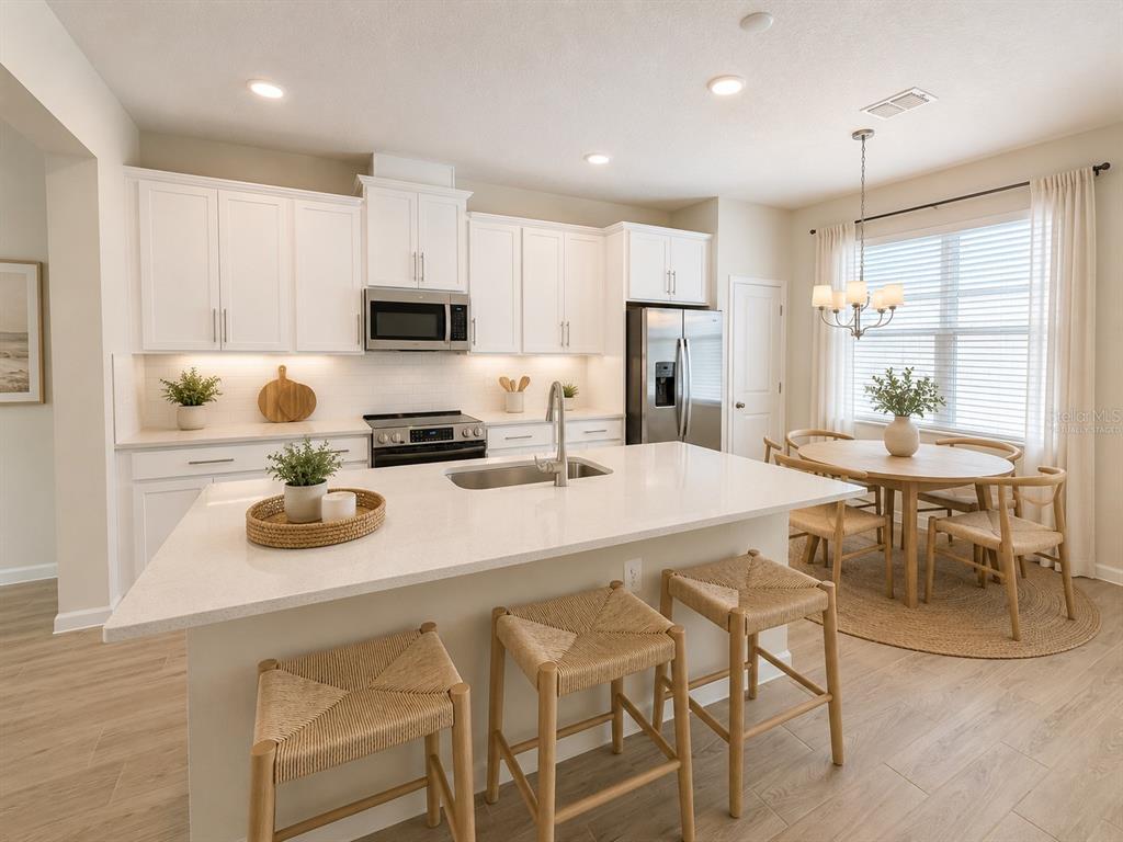 A modern kitchen features white cabinets, a large quartz island, and a dining area — 474 LADY PALM STREET, APOPKA, FL