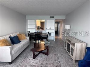 A living room features a glass coffee table, seating, and large windows overlooking the water — 300 WOODETTE DRIVE UNIT 303, DUNEDIN, FL