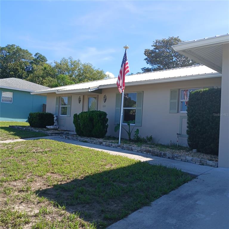 A single-story house with a light-colored exterior, a metal roof, and an American flag — 9201 N CARESSA WAY, CITRUS SPRINGS, FL