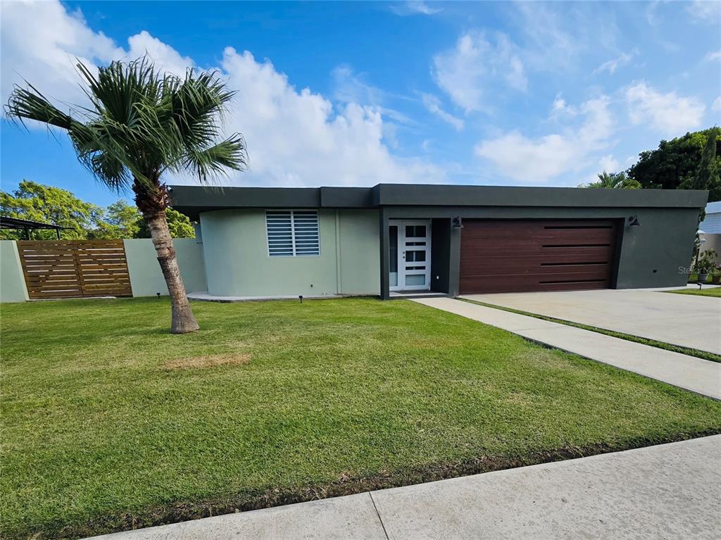 A modern single-story house with a flat roof, dark trim, and a wooden garage door — 2 ROOSEVELT GARDEN, CEIBA, PR
