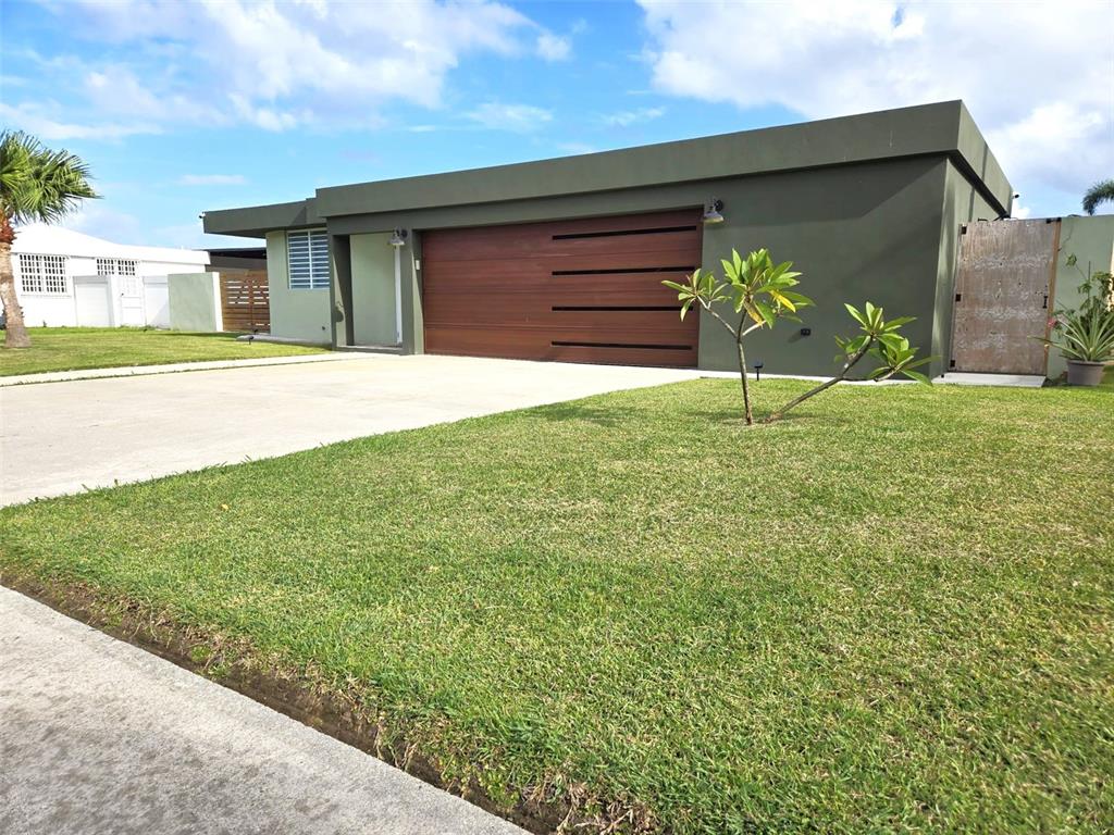 A modern, flat-roofed house with a dark green exterior and a horizontal wood garage door — 2 ROOSEVELT GARDEN, CEIBA, PR