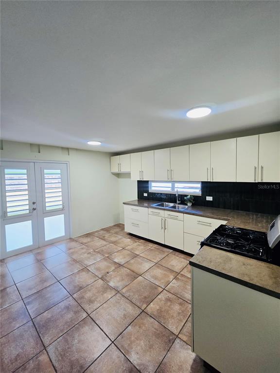 A kitchen with off-white cabinets, a dark backsplash, and brown tiled flooring — 2 ROOSEVELT GARDEN, CEIBA, PR