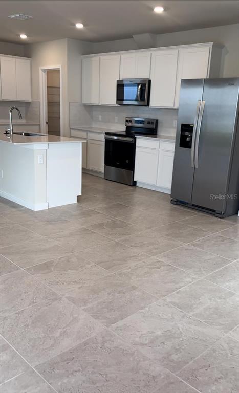 A kitchen with white cabinets, stainless steel appliances, a center island, and light-colored tile flooring — 1782 GROVELINE ROAD, ST CLOUD, FL
